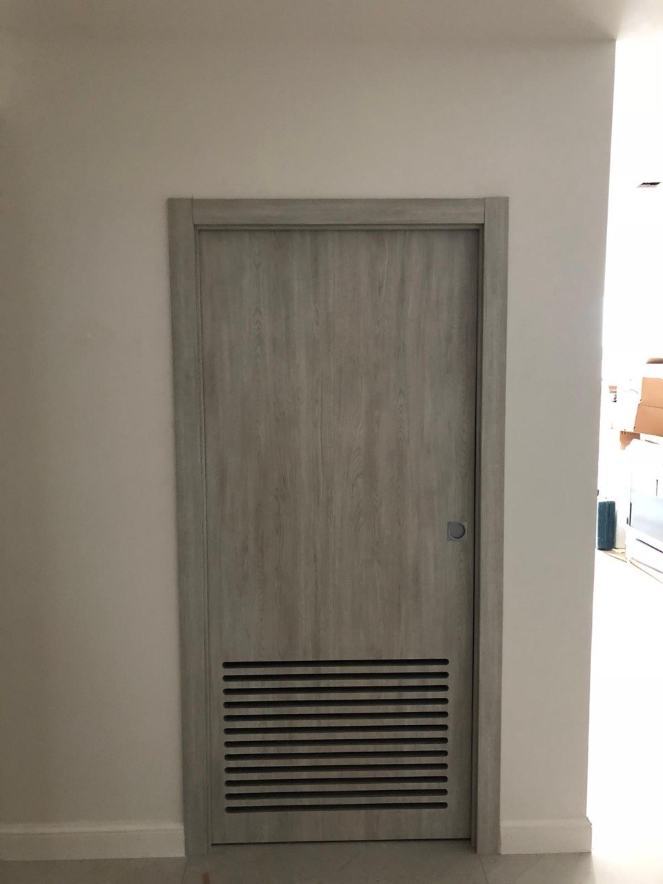 Light grey woodgrain interior door with a louvered ventilation panel at the bottom