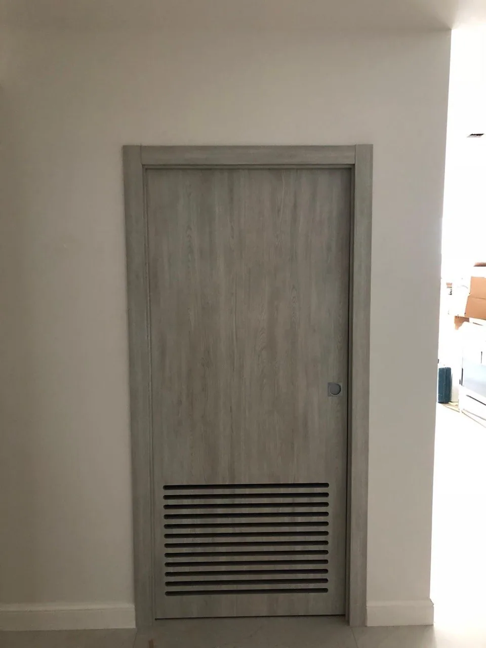 Light grey woodgrain interior door with a louvered ventilation panel at the bottom